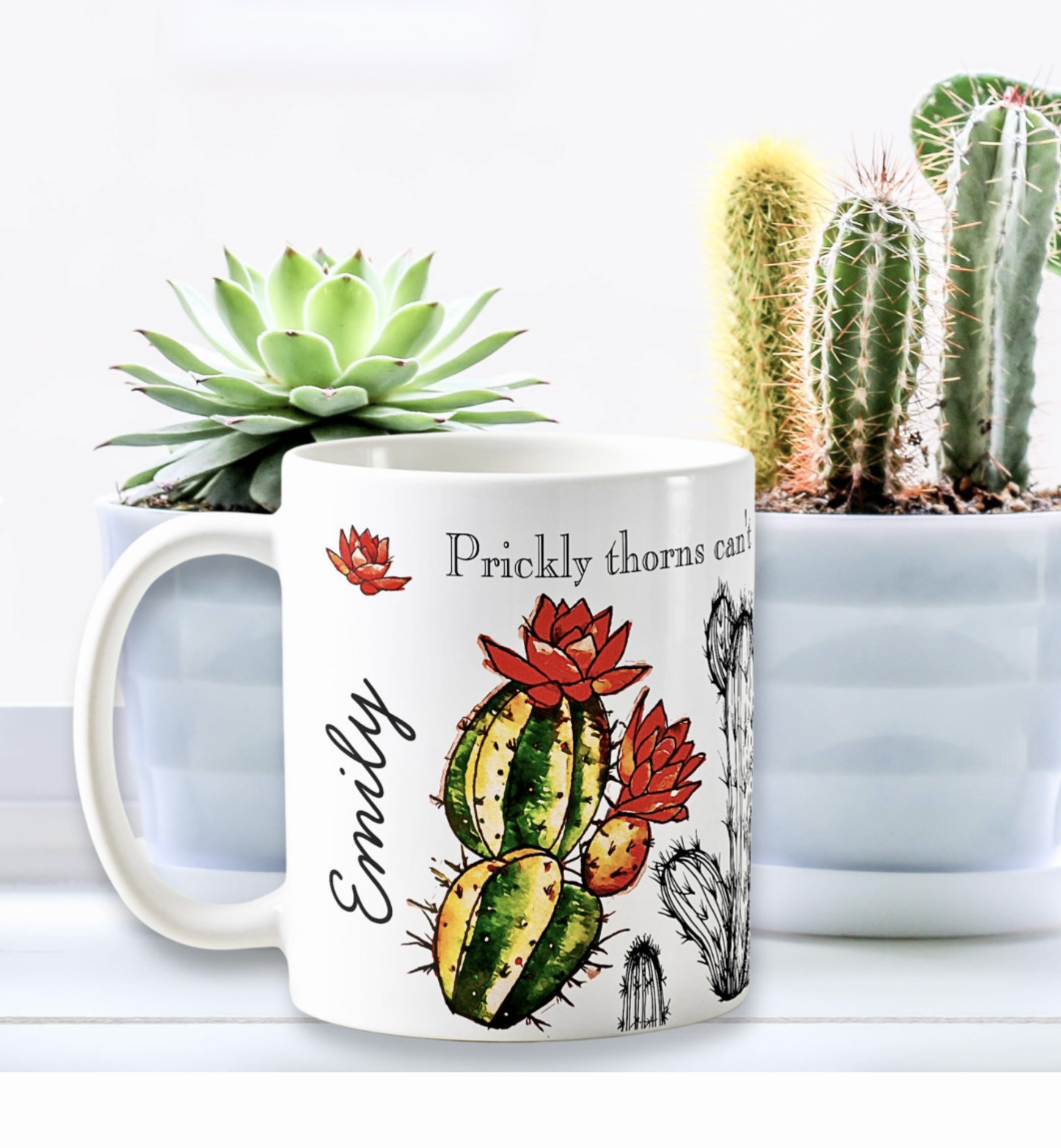 White mug with cactus images, surrounded by cacti.