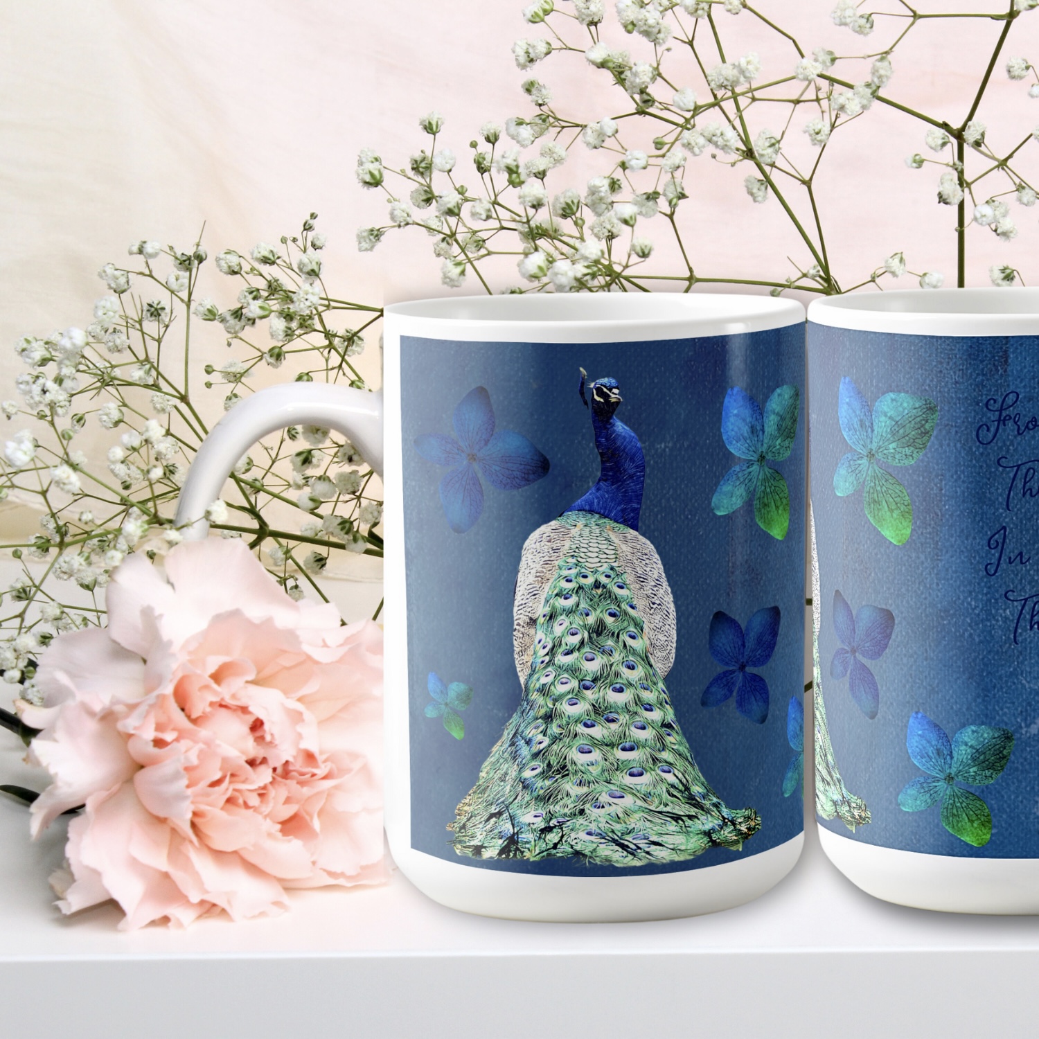 Two cobalt blue mugs, one partially shown with blue flowers. Complete mug has a blue peacock with green silver feathers. 