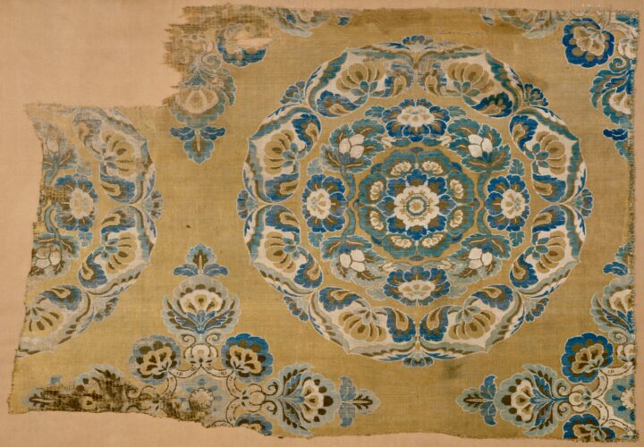 Ninth century fabric embroidery design with blue flower medallions on a mustard ochre fabric.