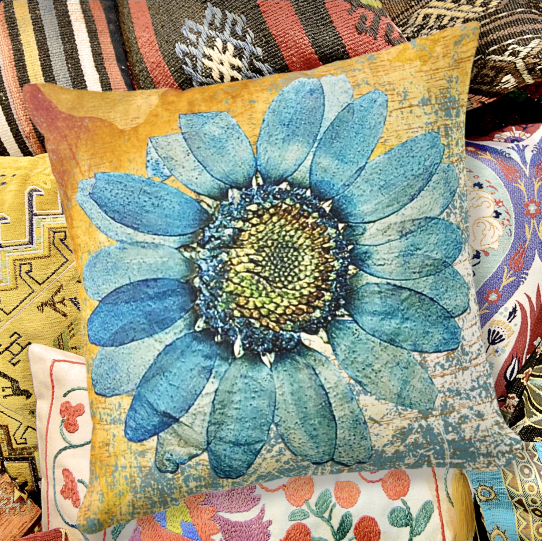 Turquoise large gerbera throw pillow with an orange ochre washed out surface, surrounded by other pillows.