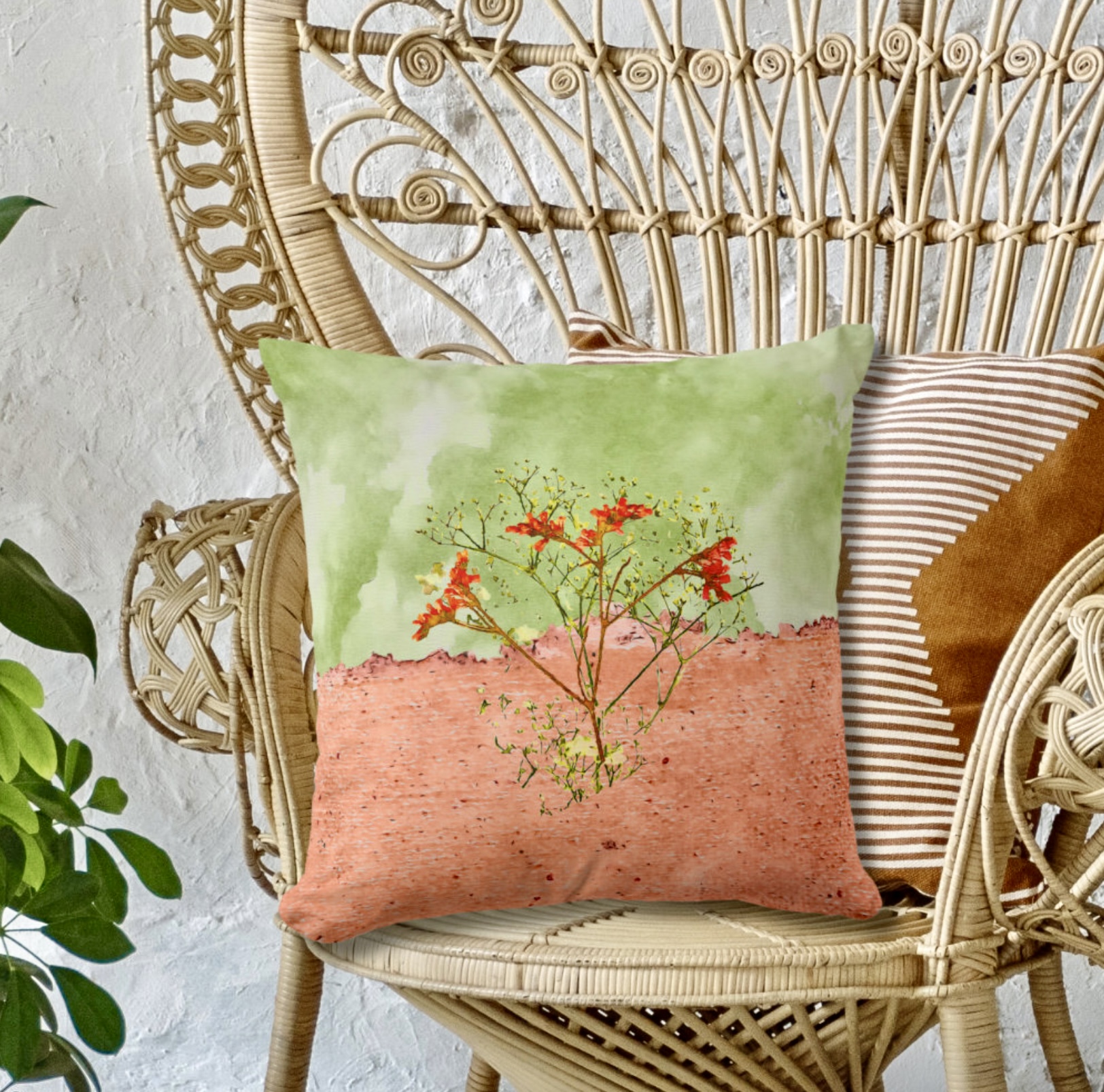 Green and peach throw pillow with orange and yellow flowers leaning on a rattan chair.