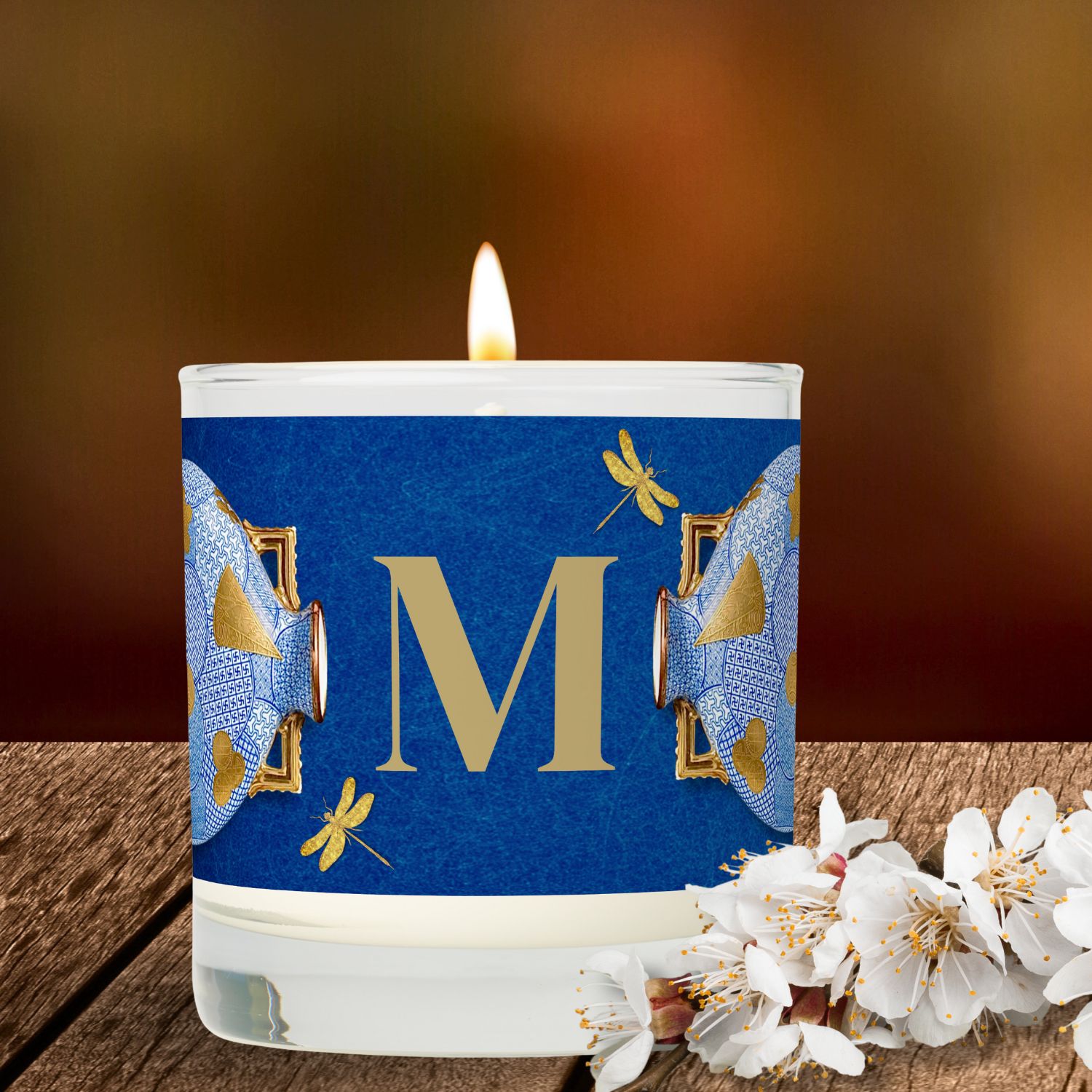 Unique luxury blue and gold scented candle, elegantly placed on a wooden surface with white little flowers on the side.