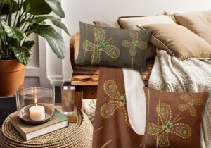 A close up image showcasing teal and brown decor featuring unique butterfly pillows and a matching blanket. The pillows and blanket are adorned with vibrant butterfly motifs in turquoise and golden hues, set against a rich brown background. The design adds a touch of whimsy and sophistication to the space, creating a cozy and inviting atmosphere.
