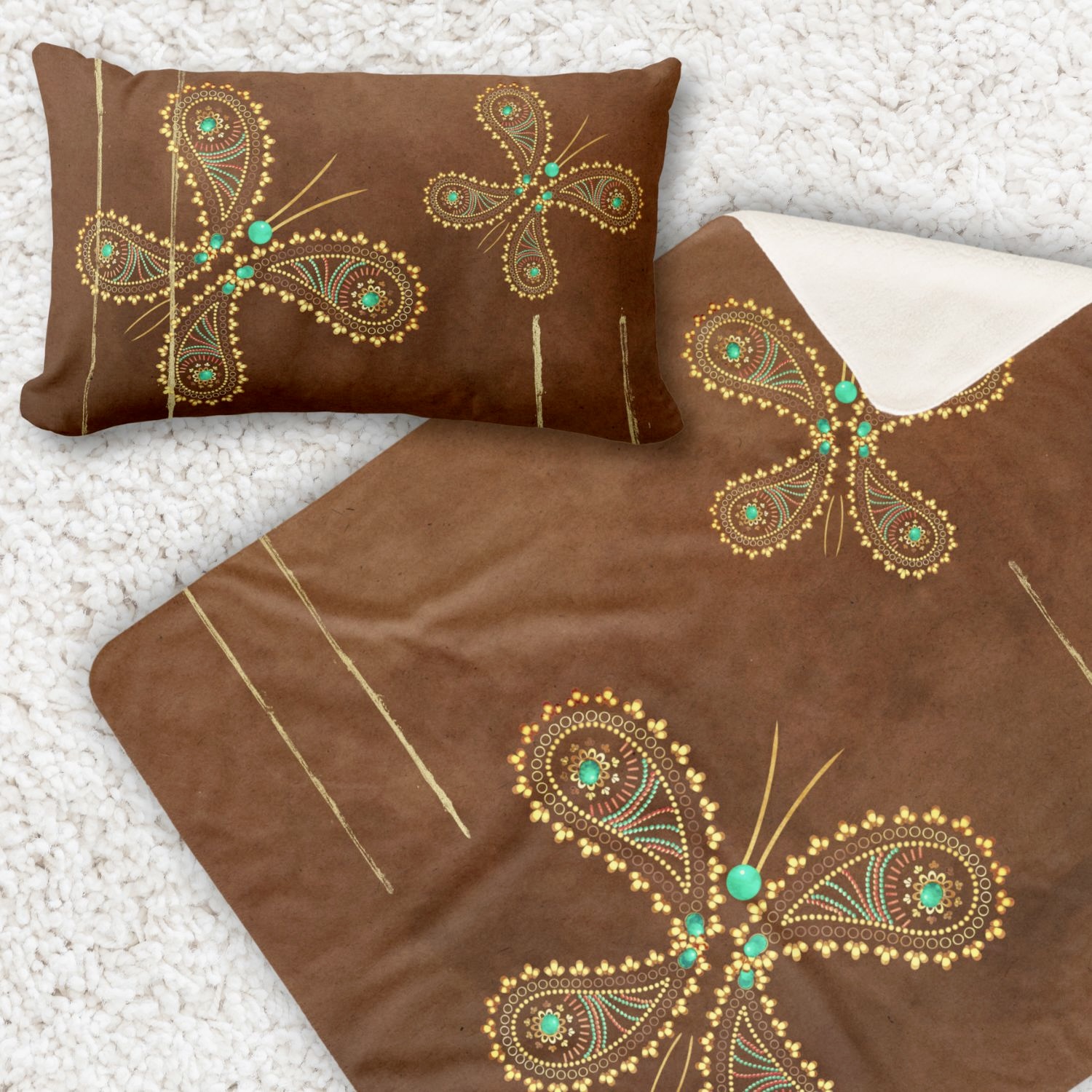 A cozy living room scene featuring a double-sided decorative throw pillow and a Sherpa blanket adorned with a teal and brown butterfly design, placed on a warm brown sofa. The intricate butterfly motifs in turquoise and golden hues stand out against the textured fabric of the pillows, adding a touch of whimsy and sophistication to the cozy ambiance of the space.