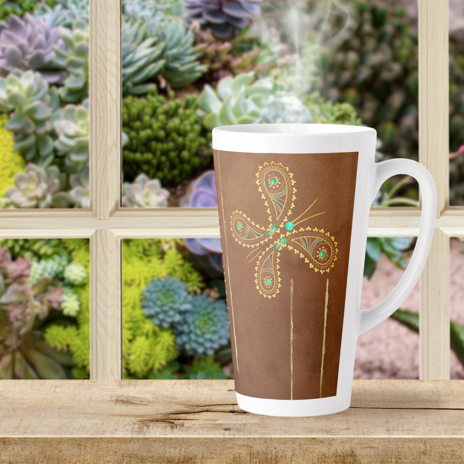 A latte mug adorned with a teal and brown butterfly design sits on a windowsill overlooking a serene outdoor scene. The intricate butterfly motifs in turquoise and golden hues stand out against the rich brown color of the mug, adding a touch of whimsy and sophistication to the tranquil ambiance of the space.