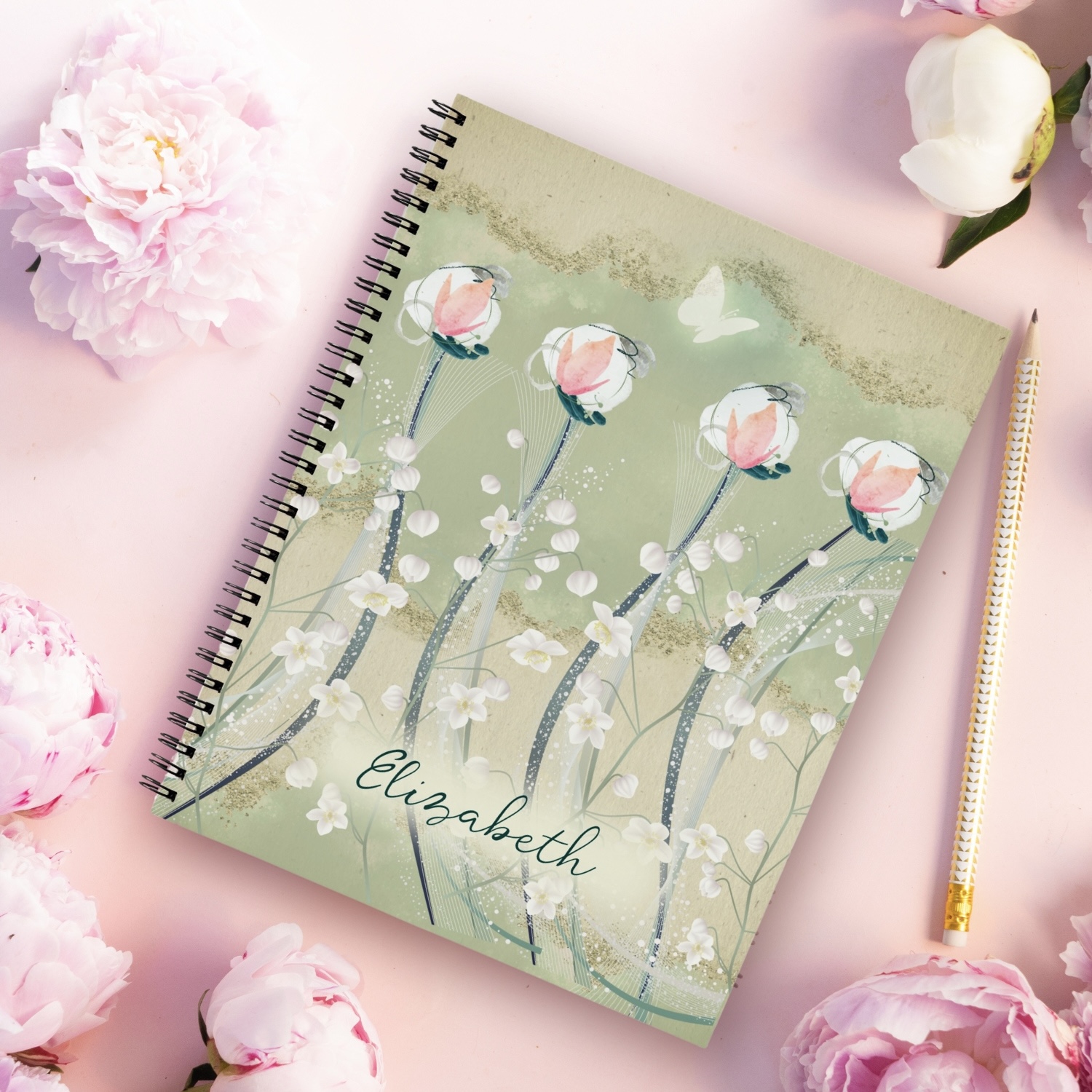 A notebook with a moss green and white floral design, featuring delicate pastel flowers and earthy beige accents. The notebook's cover includes a subtle white butterfly, adding a touch of bohemian charm. With lined pages for note-taking and a durable hardcover, this notebook is perfect for jotting down ideas or daily planning. Ideal for use in a she shed with throw pillows and mugs that reflect a boho style.
