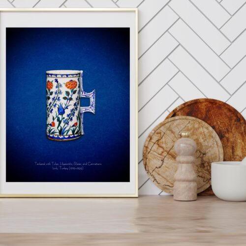 A 16th-century Iznik floral tankard poster print featuring a public domain masterpiece. The tankard is adorned with dynamic floral patterns of hyacinths, carnations, blue tulips, and red roses. Initially influenced by Chinese blue-and-white porcelain, this Iznik pottery evolved into a unique style by the 1550s, popular in Istanbul and beyond. The tankard’s size suggests it may have been used as a vase for flowers, connecting it to the natural beauty and elegance of Ottoman art.