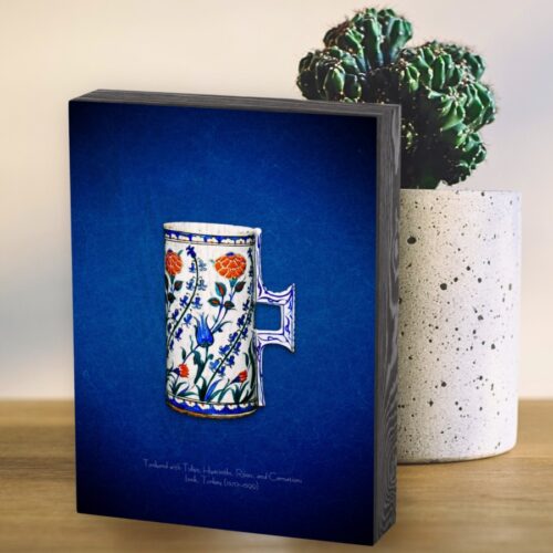 . Wooden box featuring a 16th-century Iznik floral tankard, a public domain masterpiece adorned with hyacinths, carnations, blue tulips, and red roses. The design showcases dynamic floral patterns influenced by Chinese blue-and-white porcelain, evolving into a unique style by the 1550s. The tankard, likely used as a vase for flowers, highlights the natural beauty and elegance of Ottoman art. The wooden box adds a rustic, elegant touch to the vibrant colors and intricate details.